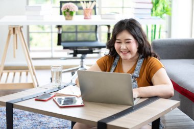 Gülümseyen tombul kadın evde çalışıyor ve bilgisayarla çalışıyor.