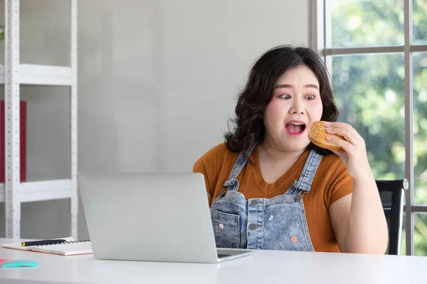 Mujer Regordeta Comiendo Una Hamburguesa Mientras Trabaja Desde Casa — Foto de Stock