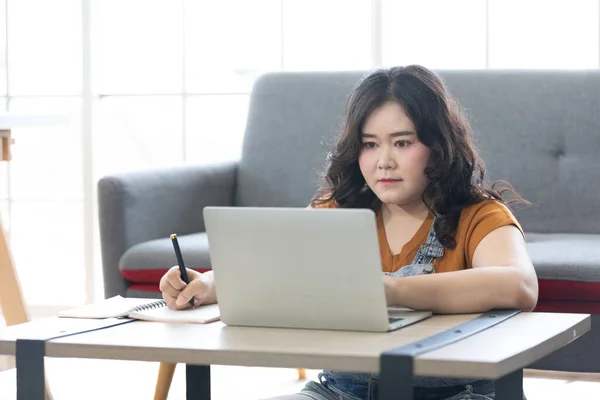chubby woman looking at laptop computer and writing on notebook for work or study