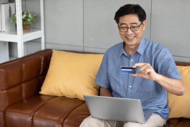 Üst düzey Asyalı adam online alışveriş yapmak ve kredi kartıyla ödeme yapmak için dizüstü bilgisayar kullanıyor.