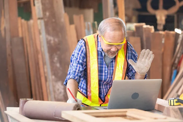 senior carpenter or worker using laptop computer and talking to someone