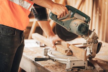 Kapalı el marangozu, atölyedeki ahşap bir parça üzerinde tahta kesmek için elektrikli testere kullanır.)