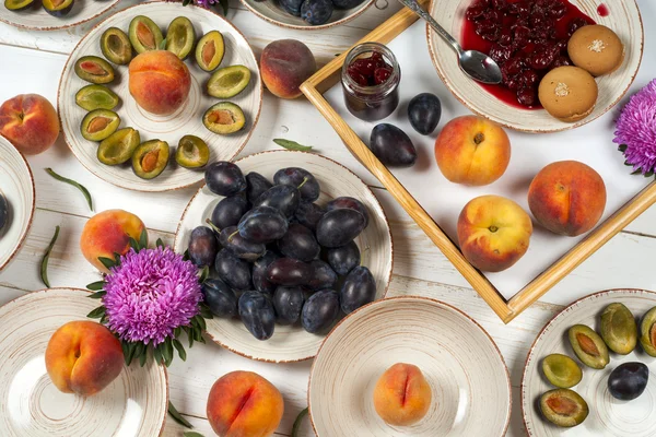 Colorful fruit set of purple, red and orange background in bowls. Plum, peaches, watermelon sliced above white tabletop