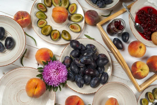 Colorful fruit set of purple, red and orange background in bowls. Plum, peaches, watermelon sliced above white tabletop