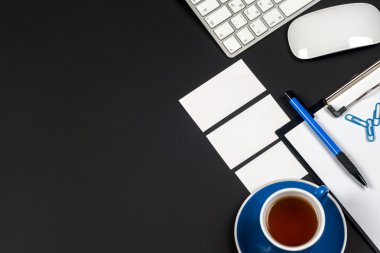 Ofis siyah resepsiyon masası beyaz bilgisayar, boş kartvizit, çiçek, kahve fincanı ve kalem.