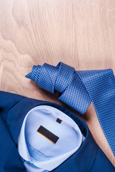 Set of classic mens clothes - blue suit, shirts, brown shoes, belt and tie on wooden background. — Stock Photo, Image