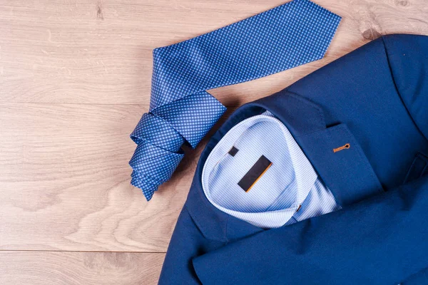 Набір класичного чоловічого одягу - синій костюм, сорочки, коричневе взуття, пояс і краватка на дерев'яному фоні . Стокове Зображення
