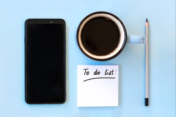 Kağıt notların yanında akıllı telefon ve bir fincan kahveyle yapılacaklar listesi. Planlama ve mesafe çalışma kavramı.