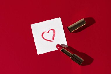 Koyu kırmızı arka planda rujdan yapılmış kalp çizimi olan kağıt bir çarşaf. Kadınsı aşk ve Sevgililer Günü konsepti.