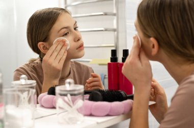 Gençlerin günlük sabah rutini. Genç kız banyoda aynaya bakıyor, yüzünü temizliyor, pamukla kozmetik tedavi uyguluyor..