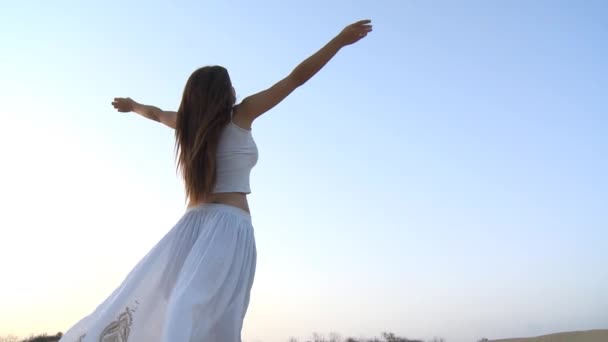 Chica con vestido blanco esparciendo sus brazos en un fondo de cielo en el desierto — Vídeos de Stock