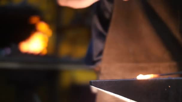 Forgeron frappé avec le marteau frappant le métal chaud sur une enclume dans un atelier derrière lui une forge 