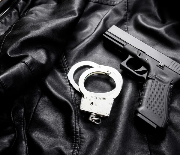 Gun with handcuffs on leather jacket — Stock Photo, Image