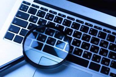 Magnifying glass on laptop keyboard  clipart
