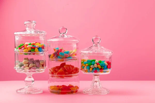 Recipientes de vidrio con caramelos sobre fondo rosa — Foto de Stock