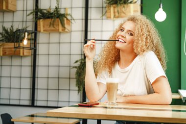 Kahve dükkanında masada oturan kıvırcık, genç bir kadın bir fincan kahveyle rahatlıyor.