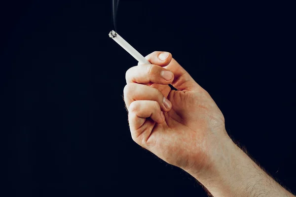 Mano masculina con un cigarrillo ardiente sobre fondo negro —  Fotos de Stock