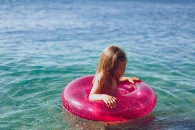 Pembe şişme dairesi olan küçük kız denizde banyo yapıyor.