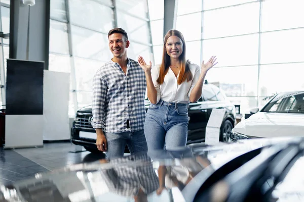 Jovem casal feliz acabou de comprar um carro novo em uma concessionária — Fotografia de Stock