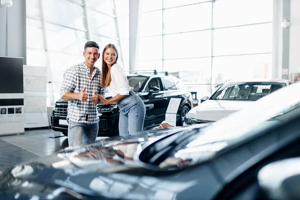 Jovem casal feliz acabou de comprar um carro novo em uma concessionária — Fotografia de Stock