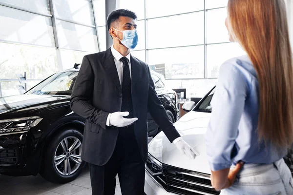 Man car salesman in face mask talking to a client in showroom