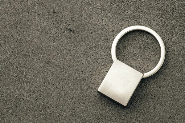 Ciondolo chiave in metallo su sfondo di cemento scuro — Foto Stock
