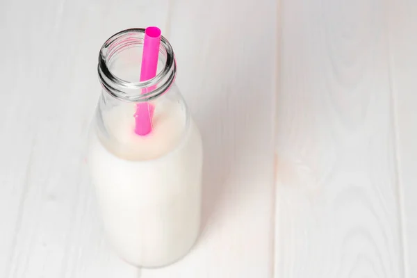 Стеклянная бутылка молока с розовой соломой на белом деревянном столе — стоковое фото