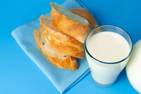 Pan de baguette fresco y jarra con leche fresca sobre fondo azul —  Fotos de Stock