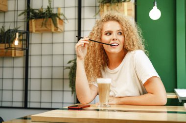 Kahve dükkanında masada oturan kıvırcık, genç bir kadın bir fincan kahveyle rahatlıyor.