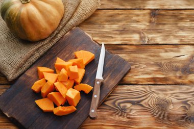 Masadaki tahta tahtada çiğ balkabağı parçaları kes.