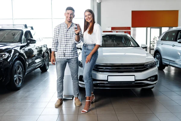 Młoda szczęśliwa para właśnie kupiła nowy samochód w salonie. — Zdjęcie stockowe