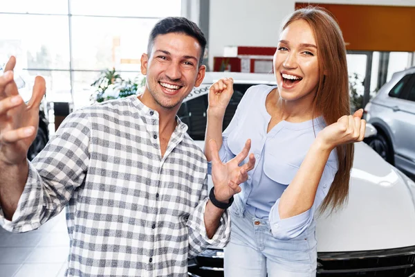 Cherrful jovem casal na concessionária comprar um carro novo — Fotografia de Stock