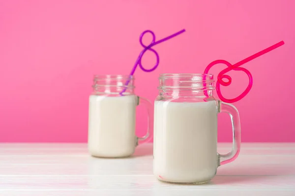 Glass jars with flavoured milkshakes against pink background — Stock Photo, Image