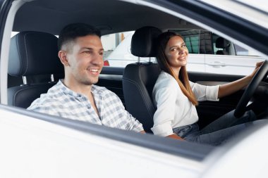 Genç bir çift araba dükkanında yeni arabalarını seçiyor.