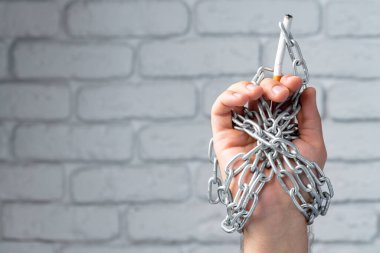 Metal zincire vurulmuş, elinde sigara tutan bir erkek.