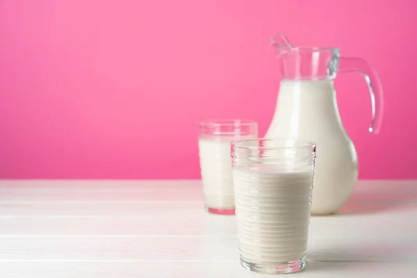 Скляний посуд зі свіжим молоком на фоні рожевого пастельного фону — стокове фото