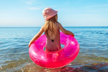 Mutlu küçük kız pembe çemberle denizde yüzüyor.