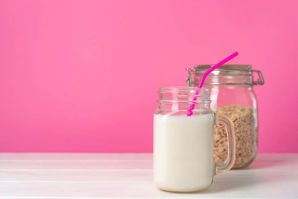 Вівсяне молоко в скляному посуді і сухі вівсяні пластівці на рожевому фоні — стокове фото