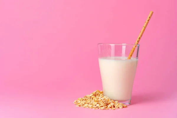 Oat milk in glassware and dry oat flakes on pink background