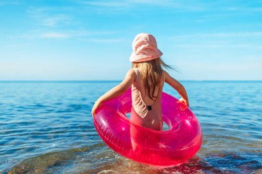 Mutlu küçük kız pembe çemberle denizde yüzüyor.