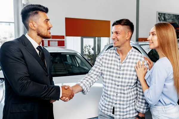 Cherrful jovem casal na concessionária comprar um carro novo — Fotografia de Stock