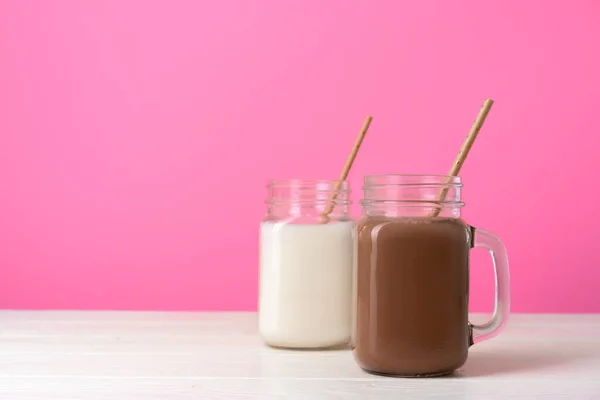 Glazen potten met gearomatiseerde milkshakes tegen een roze achtergrond — Stockfoto