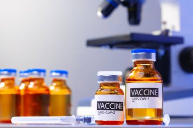 Mikroskobun yanında Covid-19 aşısı şişesi.