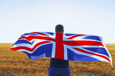 Büyük Britanya bayrağı taşıyan adam tarlada duruyor.