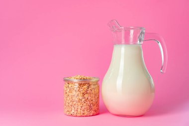 Cam kaplama yulaf sütü ve pembe arka planda kuru yulaf ezmesi.