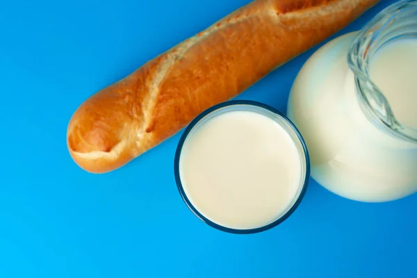 Friss bagett kenyér és kancsó friss tejjel kék alapon — Stock Fotó