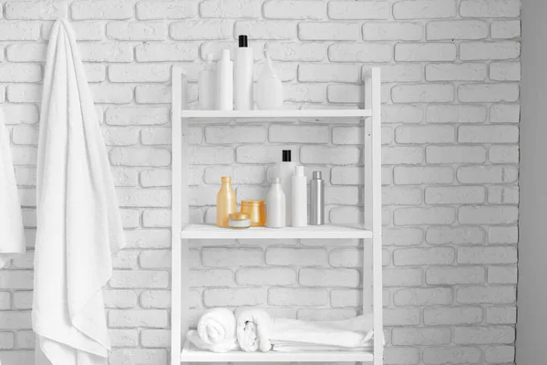 Estanterías de baño con botellas de cosméticos y toallas colgantes contra la pared de ladrillo blanco — Foto de Stock