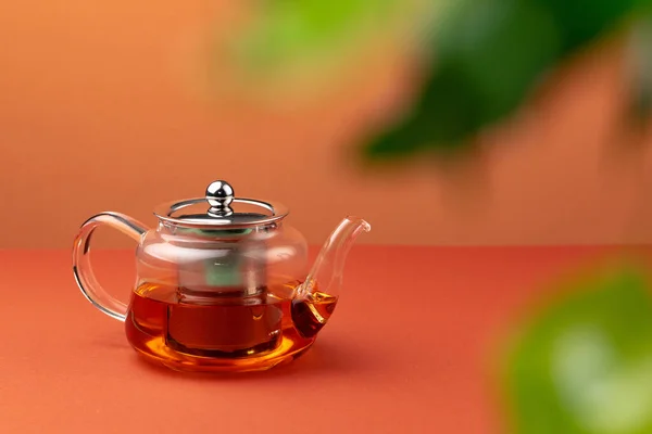 Стеклянный чайник с черным чаем на фоне размытой листвы — стоковое фото