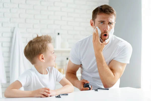 Padre enseña a su pequeño hijo a afeitarse la cara — Foto de Stock