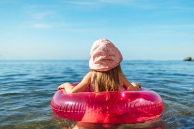 Mutlu küçük kız pembe çemberle denizde yüzüyor.